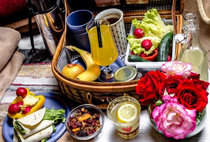 indoor picnic scene. Includes a picnic hamper of mugs, salad, fruit, soft drinks. plus on the floor wrap sandwiches, dips and a vase of roses.