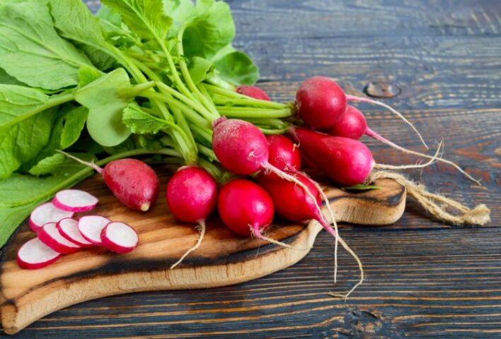 Bunch of pink radishes with green stalks an leaves. On chopping board with some sliced.