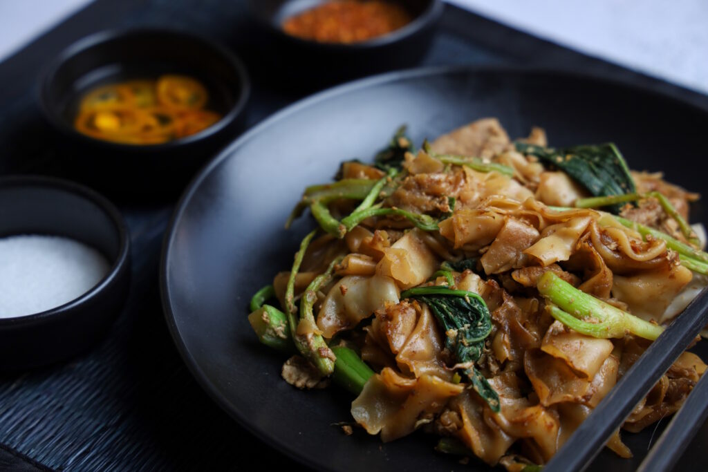Tofu and Asian Greens Pad See Ew, a stir-fried noodle dish made in the Oodles of Noodles class, featuring wide rice noodles, tofu, and vibrant greens.