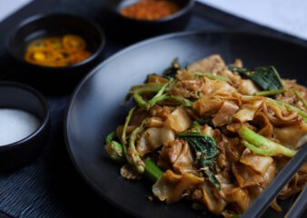 Tofu and Asian Greens Pad See Ew, a stir-fried noodle dish made in the Oodles of Noodles class, featuring wide rice noodles, tofu, and vibrant greens.