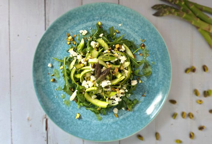 Shaved asparagus and pistachio salad served on a blue plate