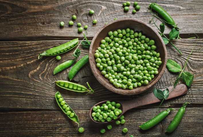 a bowl of green garden peas on a dark wooden background
